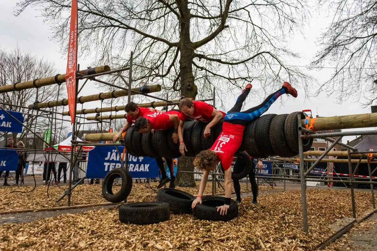 Deelnemers bedwingen een banden-hindernis boven de houtsnippers op het Raadhuisplein.